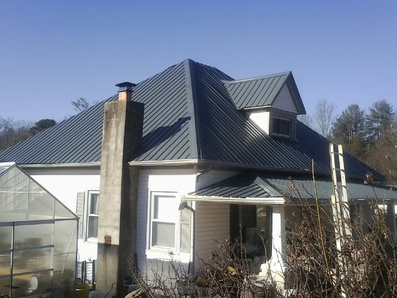 Dark blue standing seam metal roof on a white farmhouse with dormer — Slate & Tile Roof Repair by Roofing Brothers in Opelika