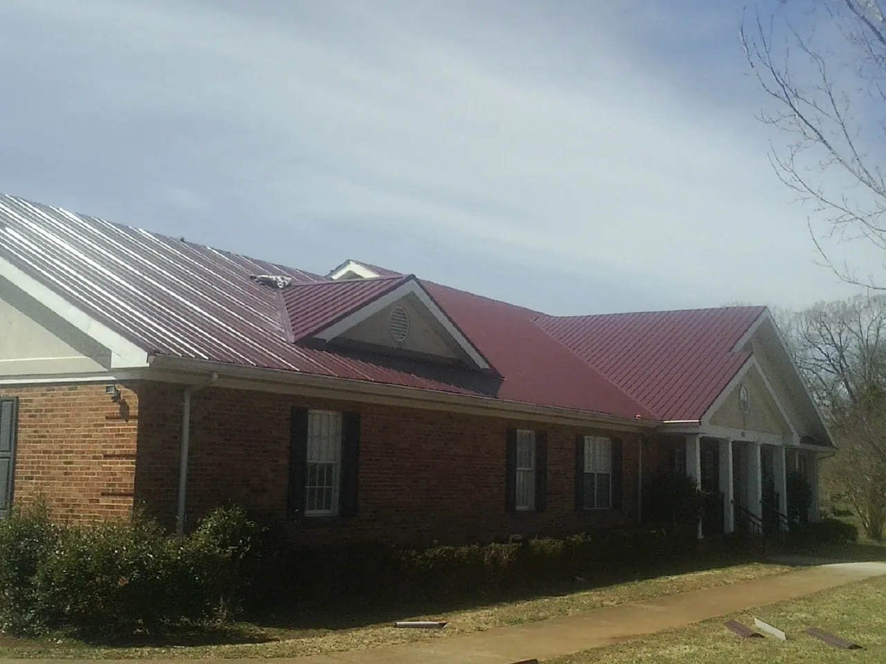 Red metal roof with gabled entries on a long brick building, from a Hail Damage Roof Repair job in Opelika