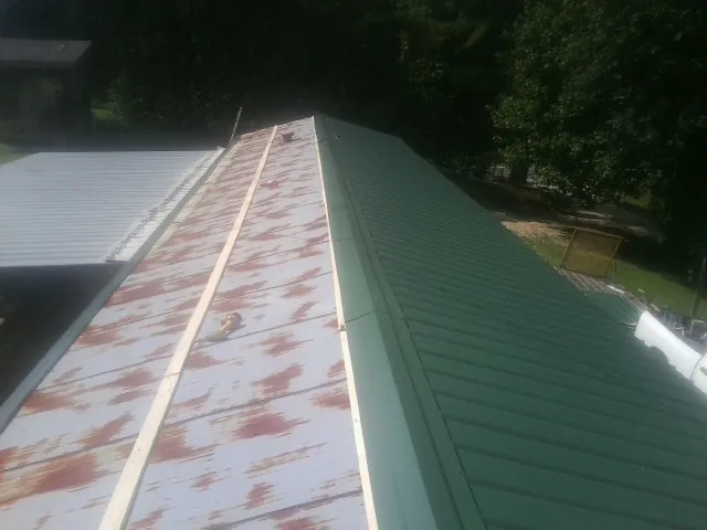 Old rusted panels beside newly installed green metal roofing — Wind Damage Roof Repair by Roofing Brothers in Opelika