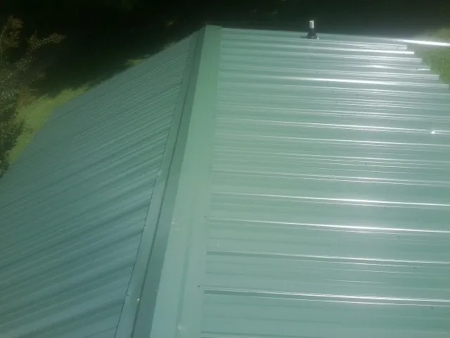 New green metal panels meeting at the ridge of a roof — Flat Roof Repair work by our crew in Opelika