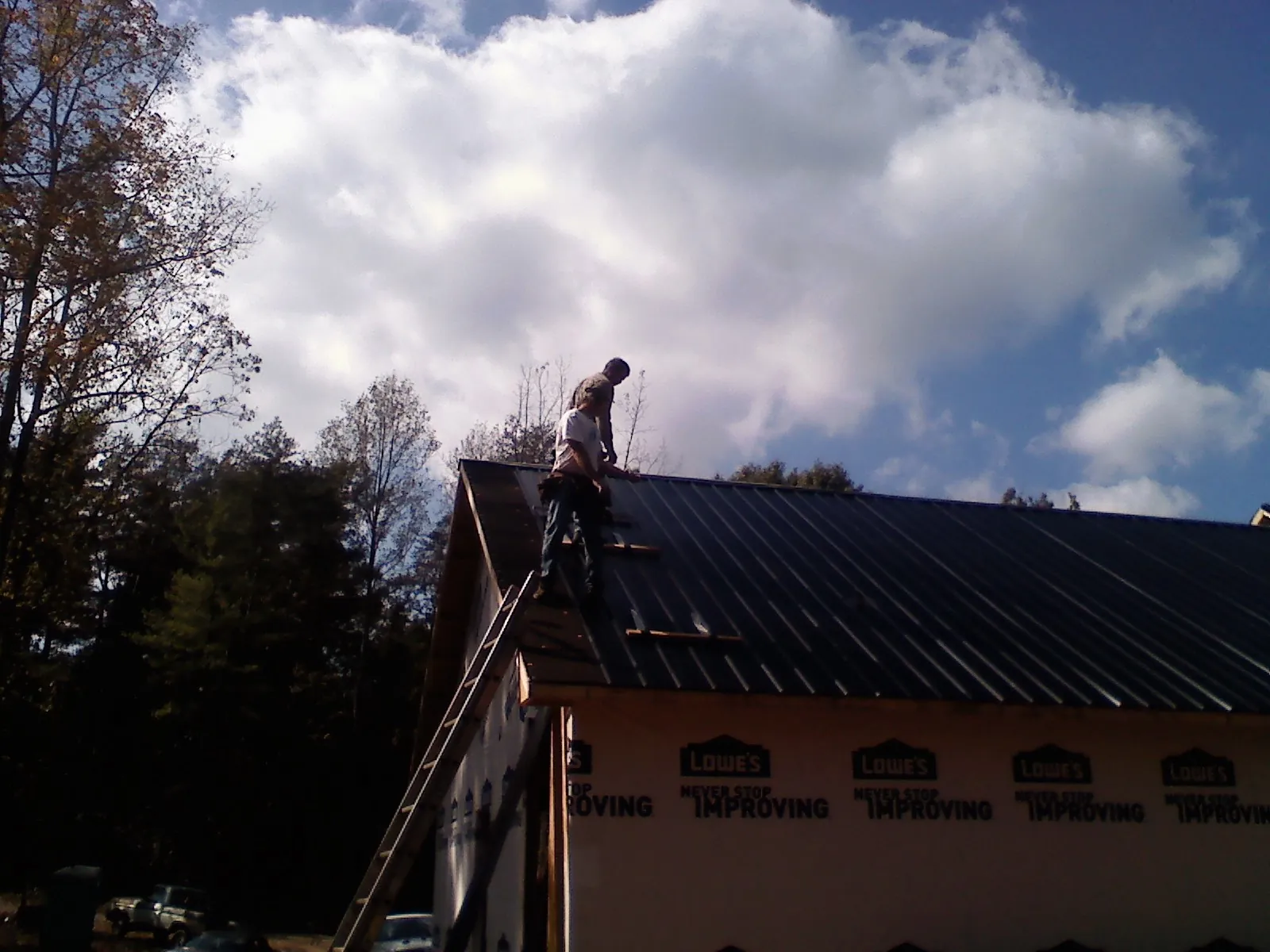 Roofer fastening dark metal panels high against a cloudy sky, from a Roof Inspection job in Opelika