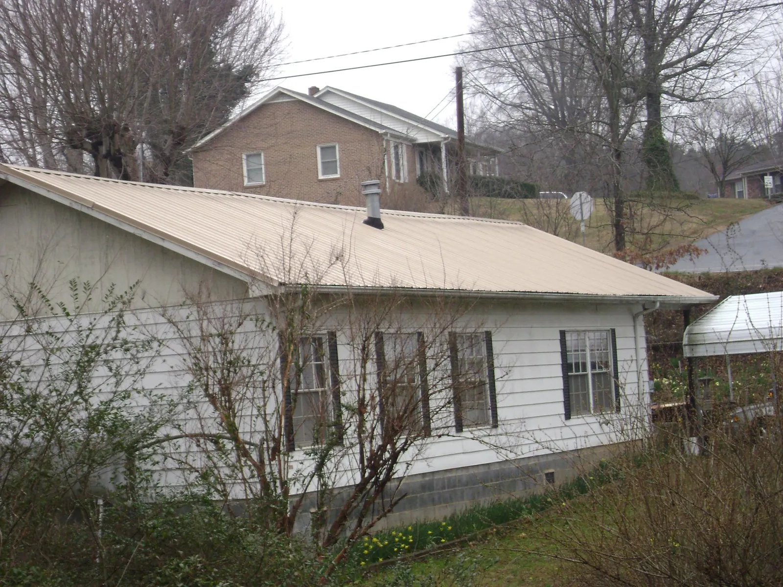 Tan metal roof on a white sided house set into a hillside — Commercial Roofing by Roofing Brothers in Opelika