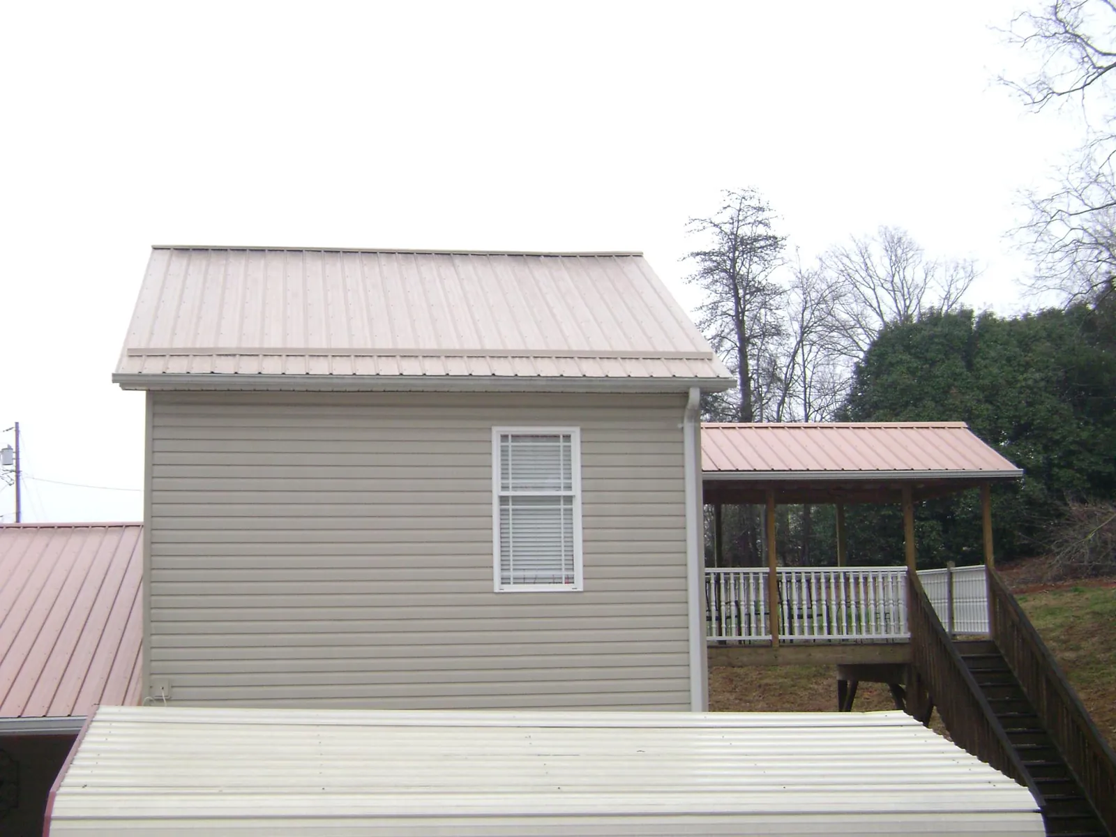 Tan metal roofs on a two story addition and attached porch, from a Roof Replacement job in Opelika